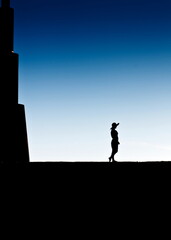 Fototapeta premium A woman in a hat is silhouetted against a blue sky, standing on a dark surface.