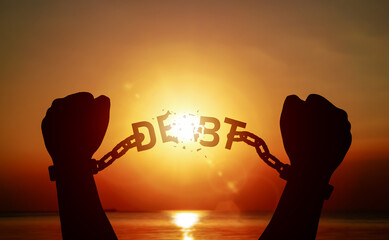 Silhouette of raised hand pulling a chain with word DEBT on until it breaks. Concept of debt relief, freedom from debt, and step towards financial stability.