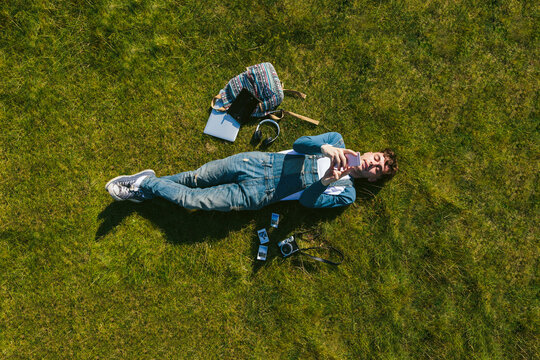 Relaxed young man lying on a meadow using cell phone, top view