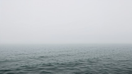 Obraz premium Mist-covered morning seascape showcasing still water and a subdued cloudy sky. Minimalist coastal view with a tranquil and empty environment. Soft natural tones creating an abstract background.