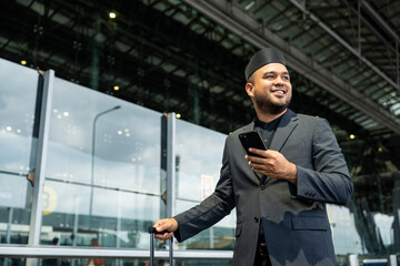 Fototapeta premium Muslim asian businessman traveler holding boarding pass ticket, passport and smartphone at the airport terminal with luggage. Cheerful tourist islamic at airport holiday trip.