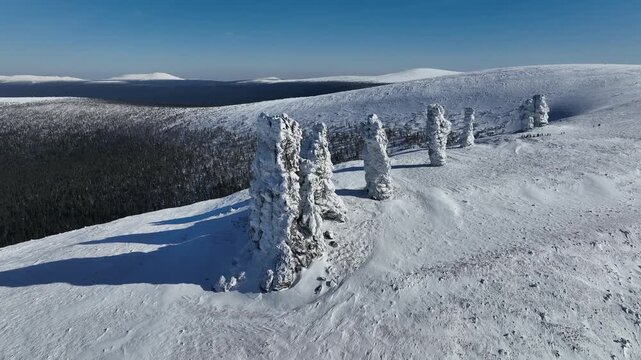 Aerial view of the snow-covered Manpupuner rock formations standing tall against the clear blue sky, showcasing the stark beauty, Komi Republic, Russia.