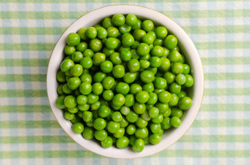 Boiled green peas in a ceramic bowl on a checkered tablecloth. Natural food concept. Vegetarian and vegan food. Horizontal orientation. Selective focus. Top view.