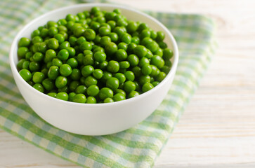 Boiled green peas in a white ceramic bowl on a checkered napkin on the table. Natural food concept. Vegetarian and vegan food. Horizontal orientation. Selective focus. Copy space