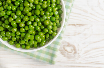 Boiled green peas in a white ceramic bowl on a checkered napkin on the table. Natural food concept. Vegetarian and vegan food. Horizontal orientation. Selective focus. Copy space. Top view.