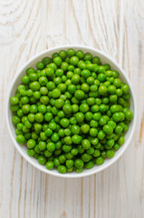 Boiled green peas in a white ceramic bowl on the table. Natural food concept. Vegetarian and vegan food. Vertical orientation. Selective focus. Top view.