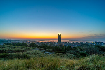 The almost rising sun colors the horizon behind the Brandaris lighthouse and the harbor on Terschelling