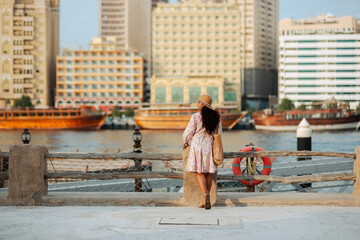 Young woman in ethnic dress and hat exploring Al Seef tourist spot in Dubai. with traditional Emirati architecture and Abra boats, she enjoys charm of Dubai Creek's cultural heritage