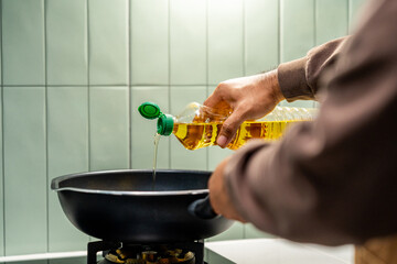 A man's hand poured vegetable oil into a pan to cook. Man's hand poured cooking oil into a hot pan, preparing to cook.