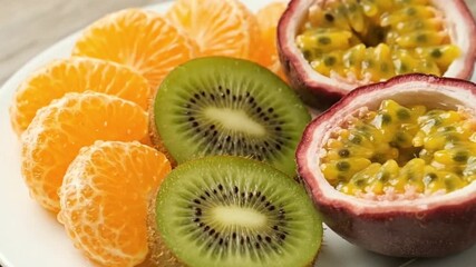 A plate featuring mandarin oranges kiwi slices and passion fruit halves arranged closely together - Powered by Adobe