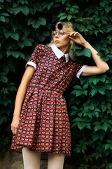 A stylish woman in a heart-patterned dress poses in front of green foliage