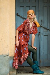 A woman in a bohemian dress, teal boots, and headscarf posing outdoors.