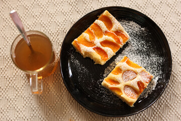 Plate with delicious apricot pie and cup of tea on table