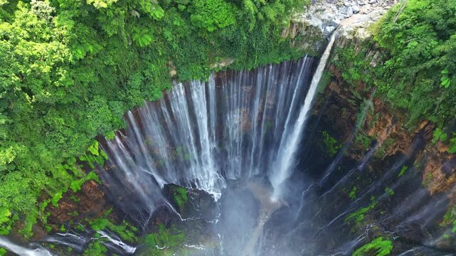 Aerial view of the majestic Tumpak Sewu Waterfall cascading down the cliff face, surrounded by vibrant green foliage, Sidomulyo, Jawa Timur, Indonesia.