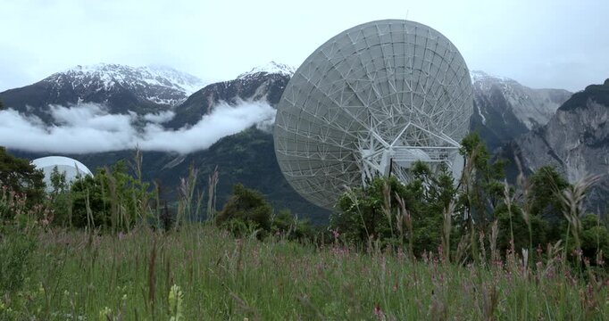 Large satellite dish captures signals in a remote mountainous region surrounded by lush greenery and clouds