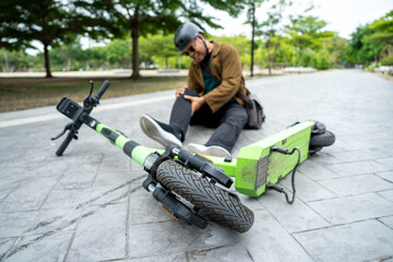 Young Asian Businessman falling off EV scooter on the road. Accident Injury leg pain. Broken leg falls off the Scooter. Accident on the road. © Chanakon