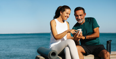Senior man and young woman using a smartphone by the sea for discussion