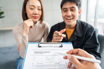 A young couple discusses life health and home insurance plans with an advisor ready to sign documents for future security and peace of mind. Meets with an insurance agent to review and sign policies