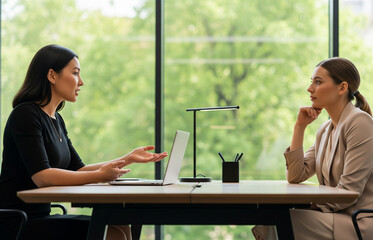Two women are having a discussion in a modern office space, seriously talking about important work at a professional desk.
