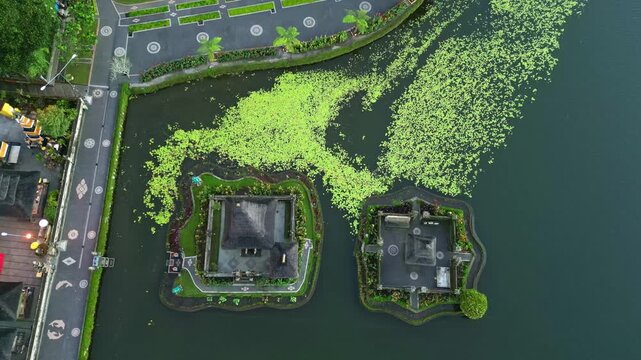 Aerial view of Danau Beratan Temple on the serene lake, with lush green vegetation contrasting against the dark water, Candikuning, Kabupaten Tabanan, Indonesia.