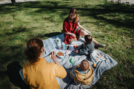 A top view of a family having a picnic on the grass, sitting on a blanket, enjoying food, sunshine, and outdoor fun in a park.