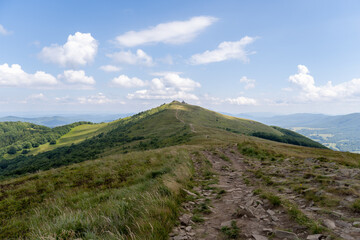 Mountain trail leading to the summit of Połonina Wetlińska with panoramic views of Bieszczady Mountains, Poland. Rocky path, green hills, and blue sky filled with clouds. © Dawid