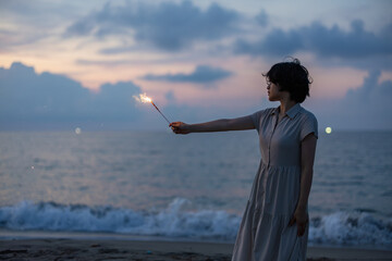 夕暮れの海辺で花火を楽しむ女性モデルの柔らかなボケ感を活かしたポートレート