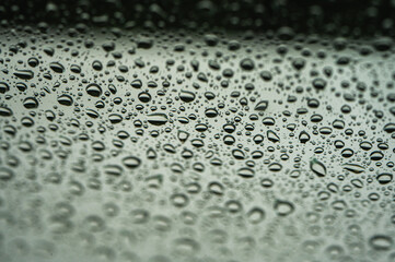 Abstract monochrome background with water drops on glass surface. Cloudy rainy weather and calm atmosphere. Selective focus, defocus