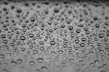 Abstract monochrome background with water drops on glass surface. Cloudy rainy weather and calm atmosphere. Selective focus, defocus
