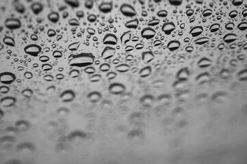 Abstract monochrome background with water drops on glass surface. Cloudy rainy weather and calm atmosphere. Selective focus, defocus