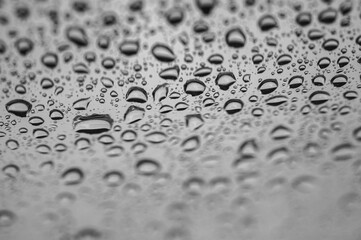 Abstract monochrome background with water drops on glass surface. Cloudy rainy weather and calm atmosphere. Selective focus, defocus