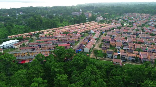 Drone orbits orderly terracotta-roof townhouses in Puerto-Princesa, contrasting the planned suburb with surrounding emerald rainforest and a bright coastal skyline under soft daylight.