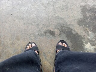 Man standing on wet concrete floor wearing sandals looking down