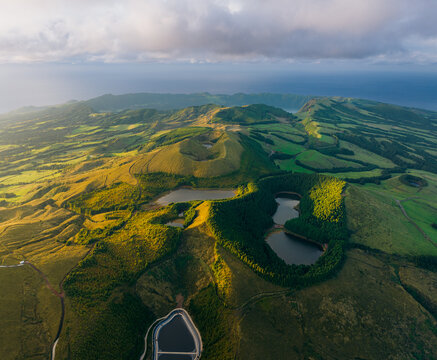 Aerial view of the vibrant green landscape, with its rolling hills and serene lakes, meeting the vast ocean under a soft, diffused light, Sete Cidades, Portugal.