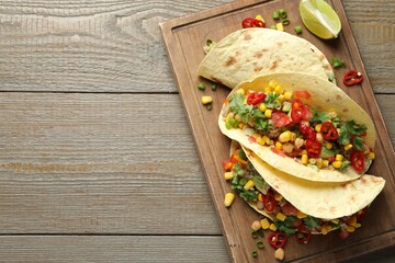 Tasty vegetarian tacos with chickpeas, corn and quinoa served on wooden table, top view. Space for text