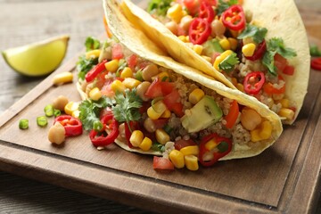 Tasty vegetarian tacos with chickpeas, corn and quinoa served on wooden table, closeup