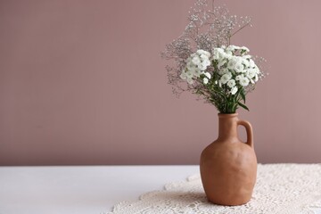 Beautiful flowers in vase on white table against pink background, space for text