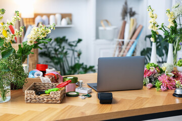 Laptop, beautiful flowers, scissors and other tools on wooden table in florist's shop