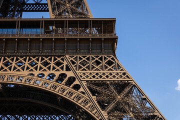 Eiffel Tower detail: ornate iron latticework, second-level platform, sunny Parisian day, architectural marvel, iconic landmark.