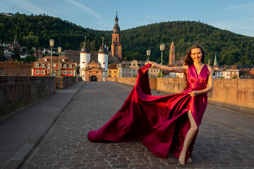 schöne Frau in rotem Kleid, tanzt in Heidelberg in der Morgensonne, über die alte Brücke.