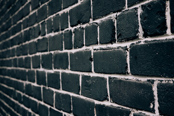 A striking black brick wall with white mortar in a detailed close-up view in perspective. A close-up view of a dark brick wall with white mortar, perfect for backgrounds and textures. Textured bricks.