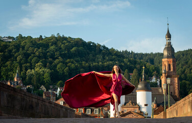 schöne Frau in rotem Kleid, tanzt in Heidelberg in der Morgensonne, über die alte Brücke.