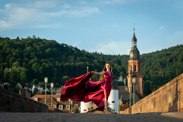 schöne Frau in rotem Kleid, tanzt in Heidelberg in der Morgensonne, über die alte Brücke.