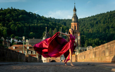 schöne Frau in rotem Kleid, tanzt in Heidelberg in der Morgensonne, über die alte Brücke.