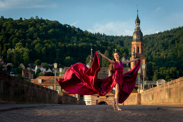 schöne Frau in rotem Kleid, tanzt in Heidelberg in der Morgensonne, über die alte Brücke.