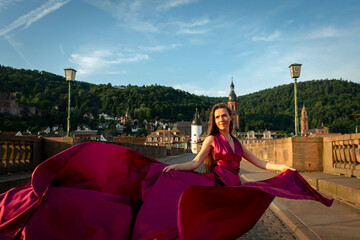 schöne Frau in rotem Kleid, tanzt in Heidelberg in der Morgensonne, über die alte Brücke.
