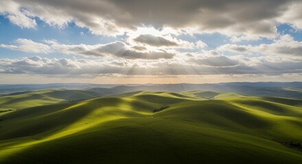 Obraz premium Rolling green hills bathed in sun rays breaking through cloudy skies