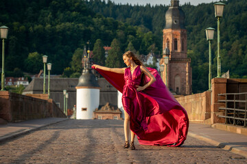 schöne Frau in rotem Kleid, tanzt in Heidelberg in der Morgensonne, über die alte Brücke.