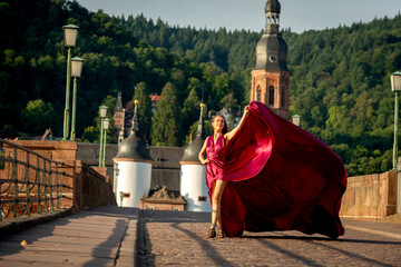 schöne Frau in rotem Kleid, tanzt in Heidelberg in der Morgensonne, über die alte Brücke.