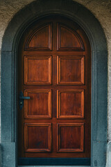 Elegant wooden entrance door with decorative panels and a dark arched stone frame located in the Swiss village of Ermatingen. The rich wood grain and traditional craftsmanship reflect timeless Europea